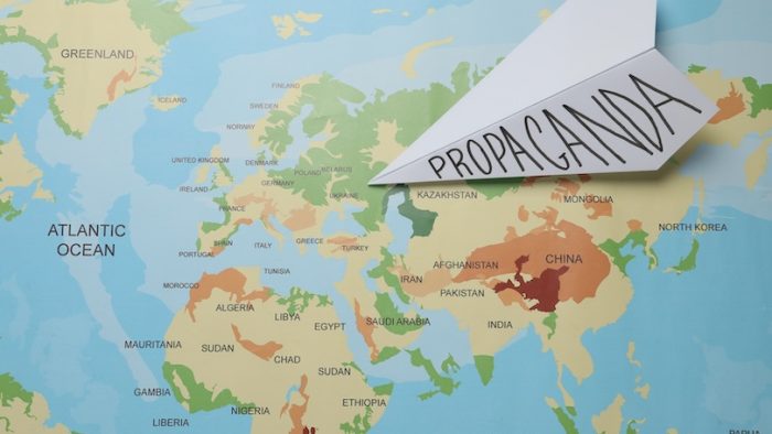 Paper airplane with word Propaganda on world map, top view. Information warfare concept