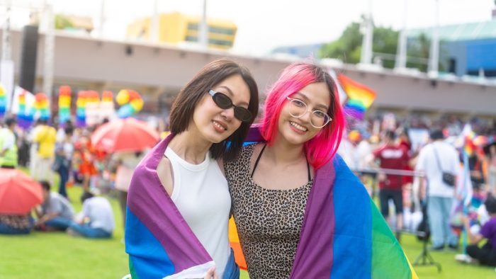 Happy young asian lesbian couple with pride movement LGBT wrapped in rainbow flag for freedom. Demonstrate rights LGBTQ celebration pride Month lesbian pride symbol. Bangkok Pride Month festival.